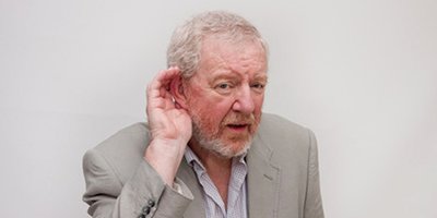 An elderly man with his head slightly tilted to the side, one hand cupped near his ears to try to hear better
