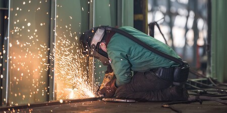 PAPR付き溶接フードを装着して研削する溶接作業者
