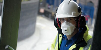 close up shot of a person wearing a safety helmet, respirator, and hearing protection
