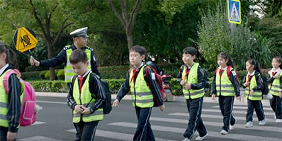 安全ベストを着た学童は、スクールゾーンの安全標識を持った大人と横断歩道を渡ります。
