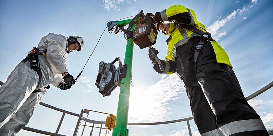 Two industrial workers in protective completing setup of confined space entry davit.
