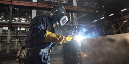 製造工場の金属構造物に溶接トーチを使用して保護具を着用する溶接工
