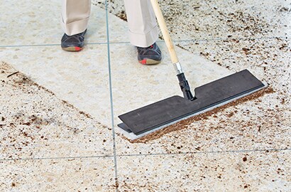A worker using 3M Easy Trap dusting tool to clean dirt off a floor.