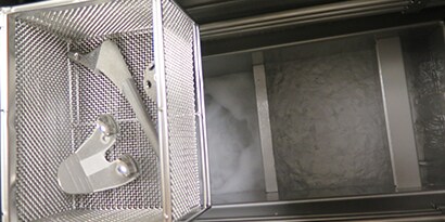 沸騰したNovec™ 73DE高機能性液体上の脱脂洗浄装置バスケットに入った整形外科用インプラントと部品の超クローズアップ。
