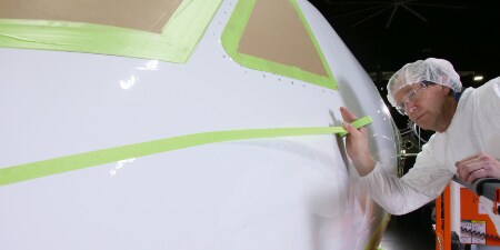 コックピットウィンドウのマスキング、および航空機の機首にマスキングテープを貼る作業者のイメージ図
