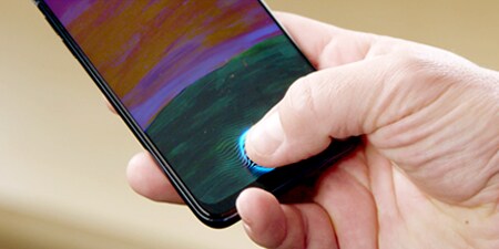 A person's hand holding a phone with their thumb touching the sensor on the bottom of the screen.

