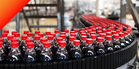 ベルトコンベアの上に置かれた何百本もの濃い色の清涼飲料水のペットボトル
