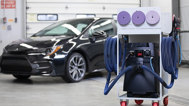 工場内で、背景に車両が見える3Mのクリーンサンディングシステム
