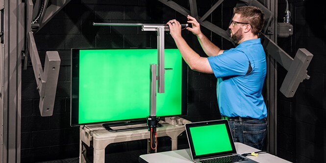 Man in blue button down shirt working with a laptop and a tv display that both have a green screen.
