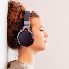 ワイヤレスヘッドフォンで音楽を聴きながら壁にもたれている女性。