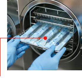 Image of gloved hands removing a tray of instruments from an autoclave