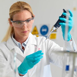 ピペットで液体を移す、白衣と手袋を着用した女性