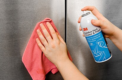 Close-up of hands using 3M Stainless Steel Cleaner & Polish on stainless steel surface.