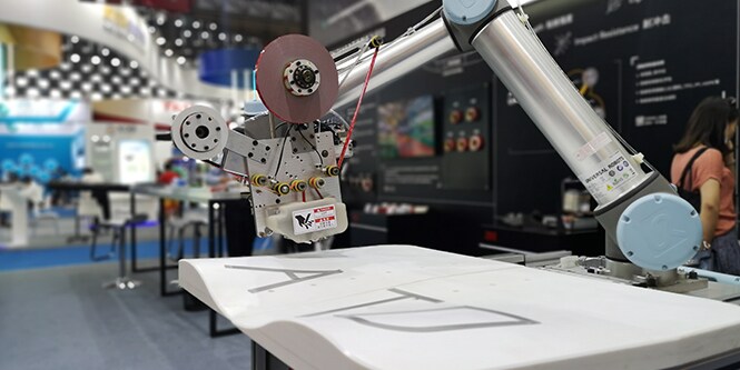 縦方向の深さが変化するワーク上に配された、アプリケータヘッド搭載のロボットアーム、画像
