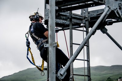 A man wearing a safety helmet, hearing protection, and a fall protection harness while working on a high location
