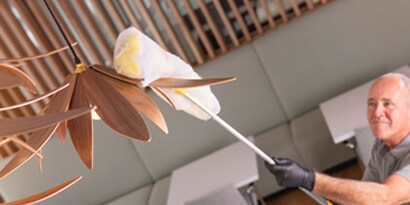 man using a high dusting tool wrapped with a 3M easy trap sweep and dust sheet to clean a commercial pendant light
