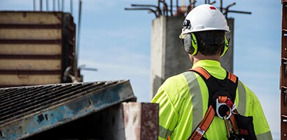A man wearing a safety helmet, harness, and hearing protection earmuffs
