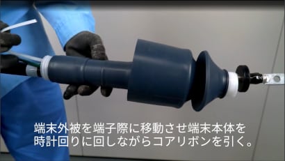 手袋をした人が3M™ PST端末耐塩用-EM（圧着端子仕様）T6PS-Bシリーズの円筒形電気部品を扱い、慎重に回転させて組み立てを示しています。

