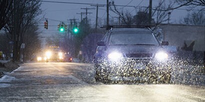 車のヘッドライトは、夕暮れ時に道路に降る雪を照らします。
