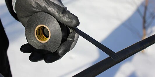 An image of a gloved hand wraping a rod in electrical tape

