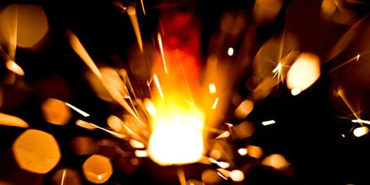 A close up image of a flame with sparks flying out of it

