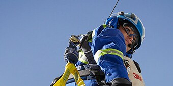 保護メガネ、ヘルメット、安全ベスト、聴覚保護具を着用し、ハーネスで空にぶら下がっている作業員

