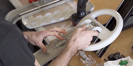 A man working on a plastic component that looks like a steering wheel of a car
