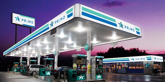 Gas station with illuminated exterior signage and purple sky in background.
