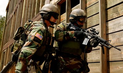 Two soldiers wearing helmets, eye protection, and full combat gear

