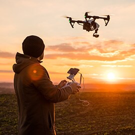 屋外で両手式のリモコンを使用して、上空のカメラ搭載ドローンを操作する男性。
