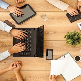 木製テーブルの上で電子機器を使用する人々の手のクローズアップ