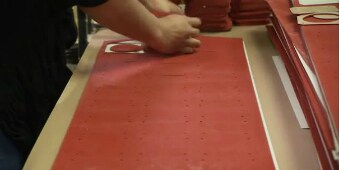 Video still of a worker removing items from a sheet of converted pieces
