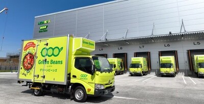 緑の配送トラックが倉庫前に並ぶ